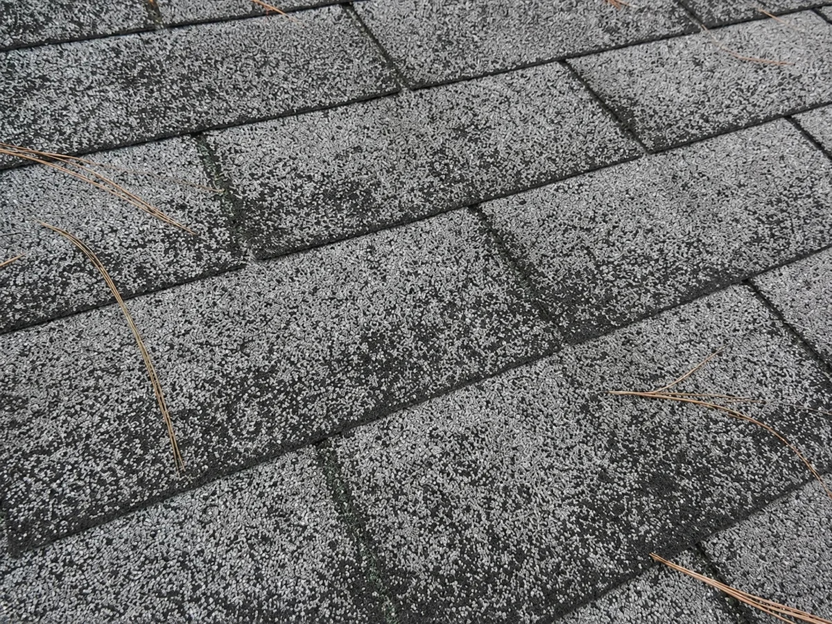 Close-up of asphalt shingles worn patchy and pale from granule loss